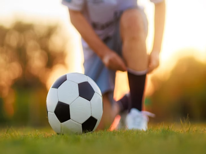A soccer ball rests on the grass while a person kneels beside it