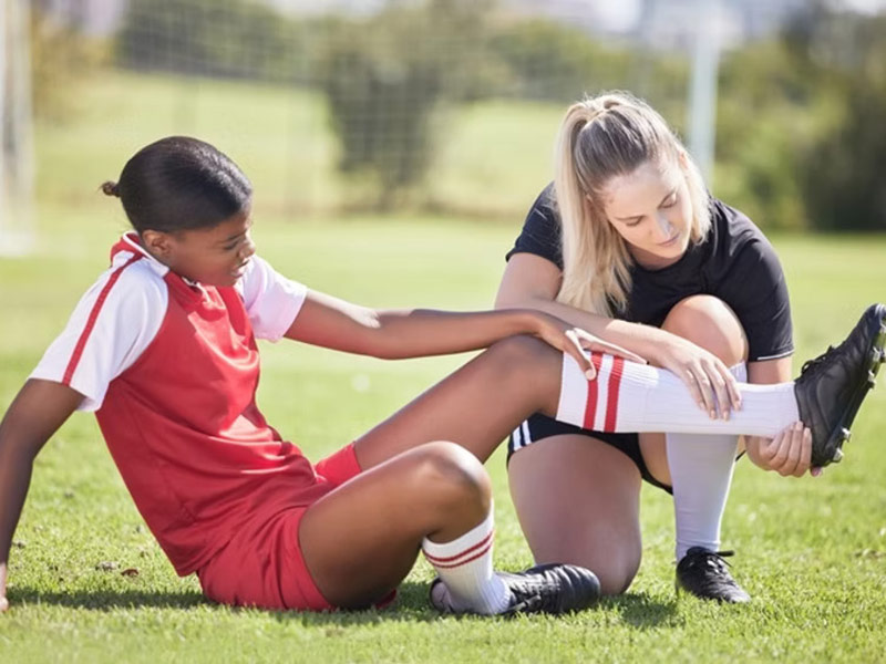 One female soccer player examines the leg of another female player